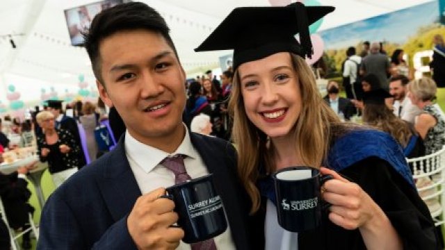 Male and female graduate holding Surrey mugs