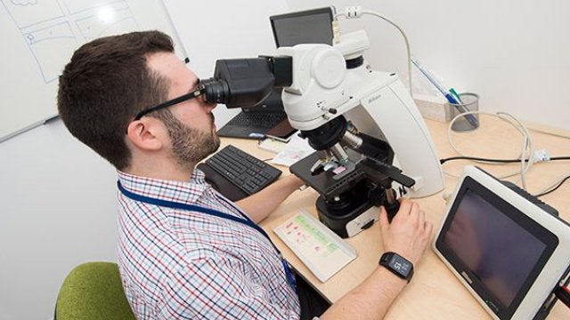 A man in a checked shirt looking into a microscope