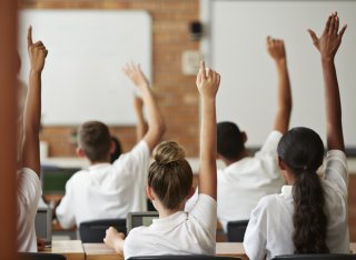 children with hands up in classroom - GETTY IMAGE
