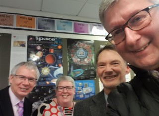 Four people in a classroom with space-related posters behind them