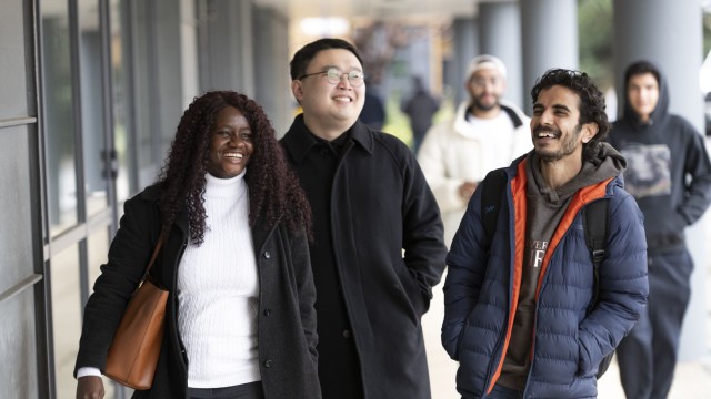 Three international students smile as they walk towards Surrey Business School