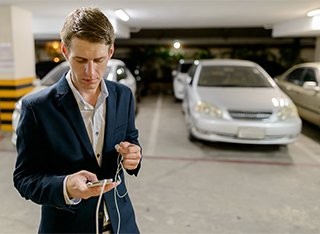 A man is looking at his phone in front of a silver car