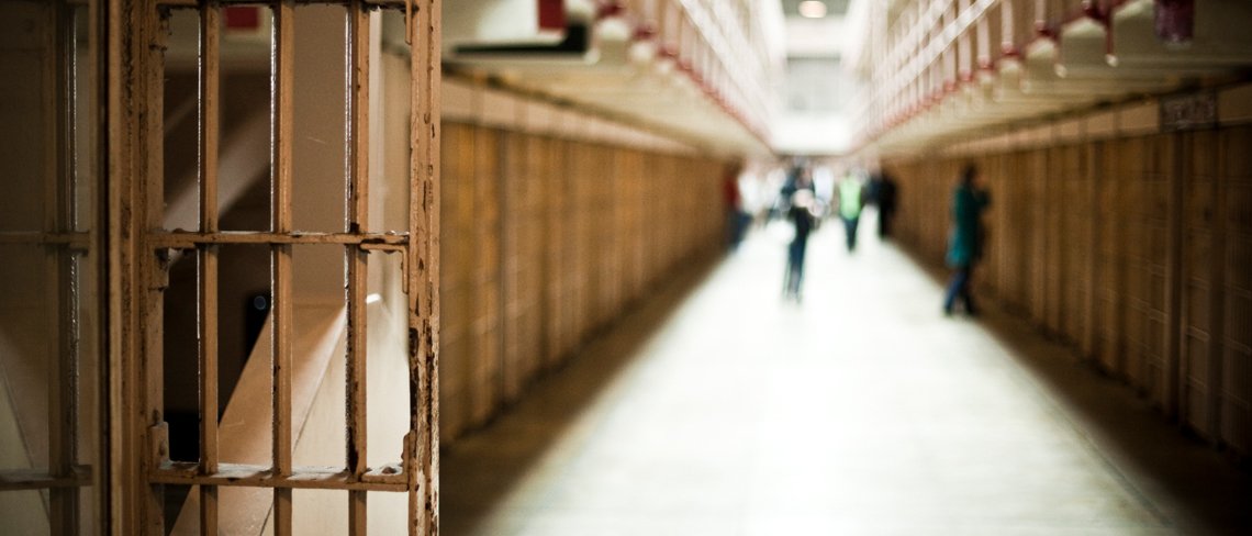 Inside a prison with people walking through between the cells.