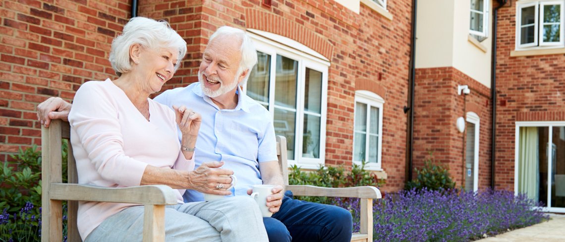 An elderly couple sitting down drinking tea and smiling