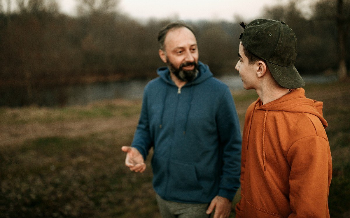 A man and boy talk as they walk through a green space