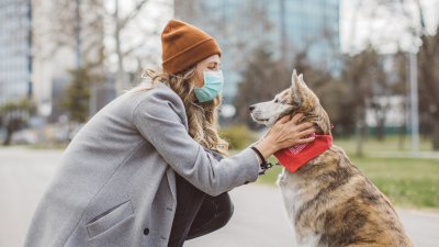 Woman wearing a PPE mask bent down petting her dog