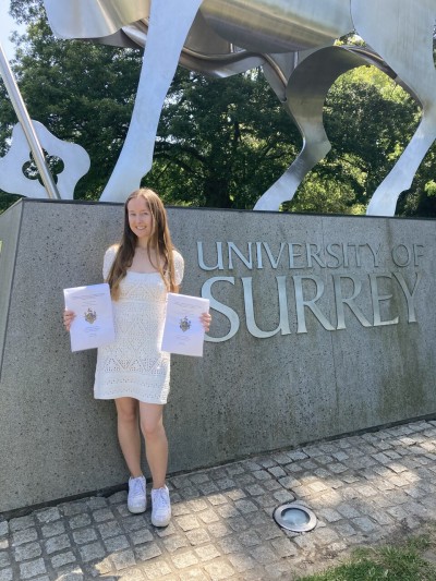 Carla, a University of Surrey Translation, Interpeting and AI MA student standing by the University's statue of its stag