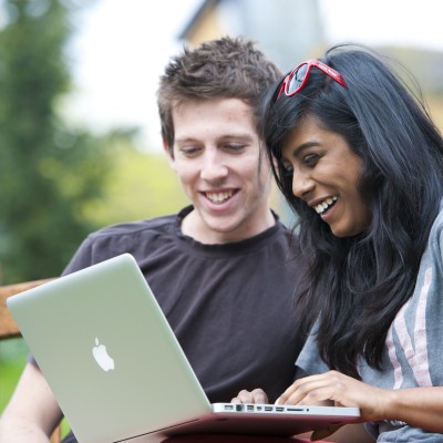Students outside campus on bench with laptop