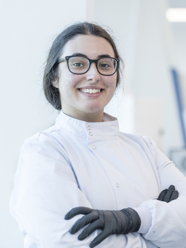 A biosciences student wearing glasses smiles confidently at the camera with her arms crossed.