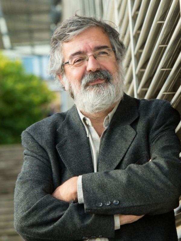 Claudio leans against a building with his arms crossed, smiling at the camera.