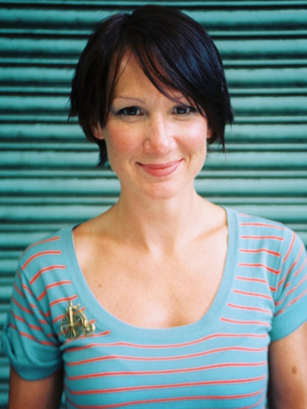 Aleks stands in front of a green background, smiling at the camera.