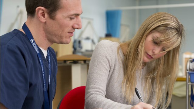 A man looking at a woman filling in a form