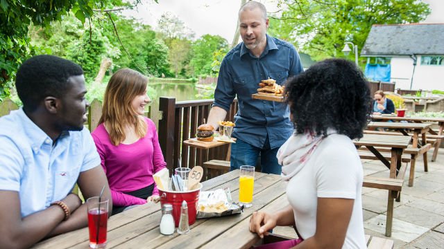 A waiter serving food to three people at a pub
