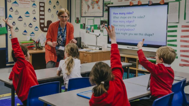 Young children in a school classroom raising their hands