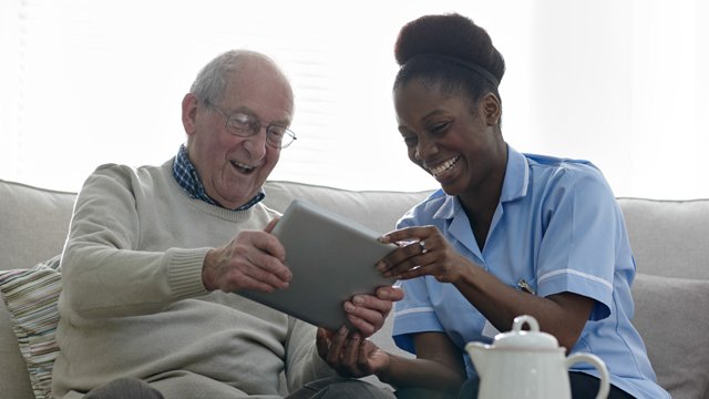 Elderly man using a tablet alongside nurse