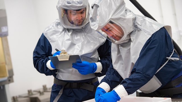 two men in hazmat suits are working in the containment level 3 room