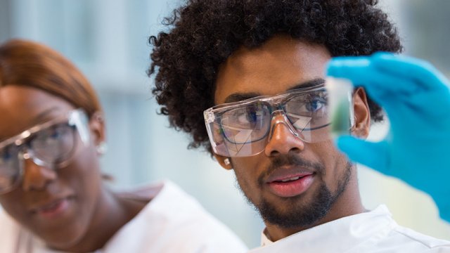 A student wearing blue gloves is holding up a perti dish