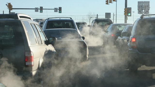 Cars in traffic with fumes coming out their exhausts