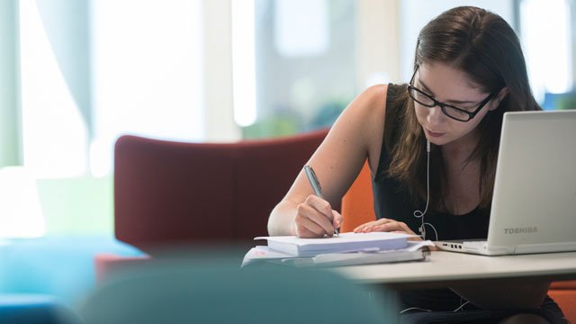 Female student studying the Library writing in a notebook