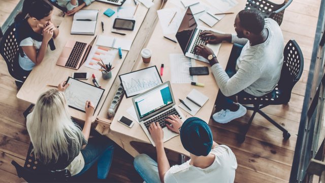 Group of young people sitting around a table working on laptops