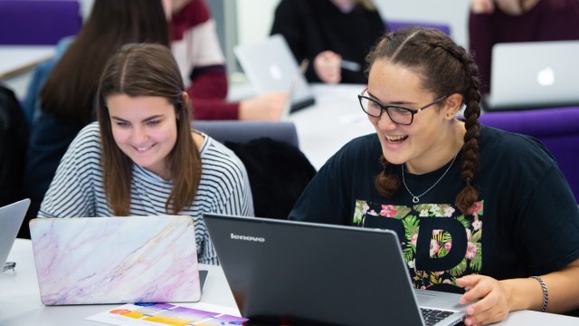 Two students on laptops laughing