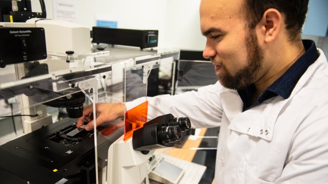 Student in lab coat standing by a microscope using scientific equipment