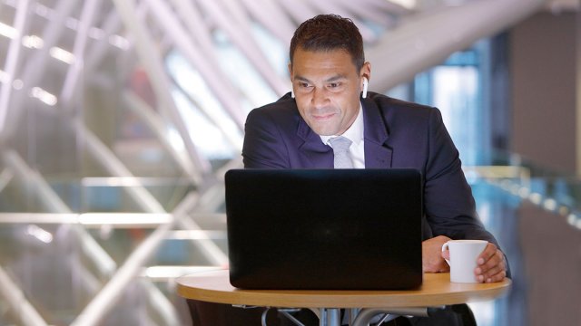 Man in a suit sat at a table and watching something on his laptop
