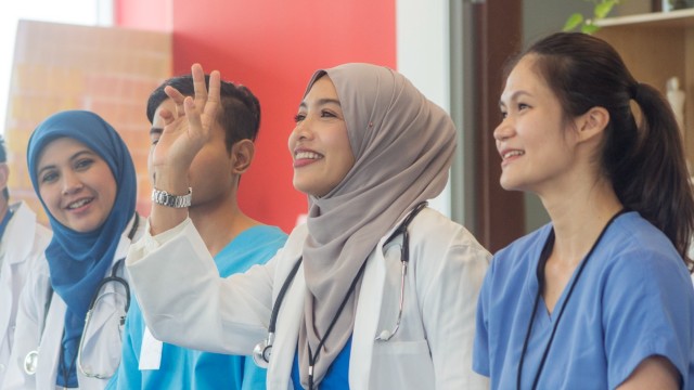 A group of Malaysian medical staff having a meeting. It is a medical team with four people from different ethnic backgrounds attending a medical conference. A Muslim female doctor raises her hand