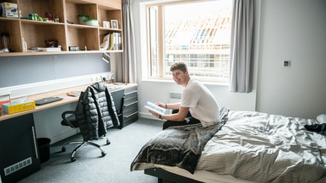 Student in university accommodation sitting on bed