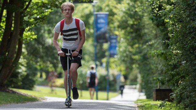 Student riding on scooter on campus