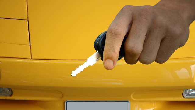 Image of person holding a car key in front of a yellow car