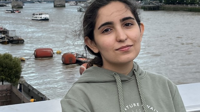 Melika, a young Iranian woman, smiles at the camera with Tower Bridge in the background.