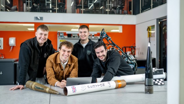 4 members of the University's Peryton Society are smiling in front of rockets they have engineered and built