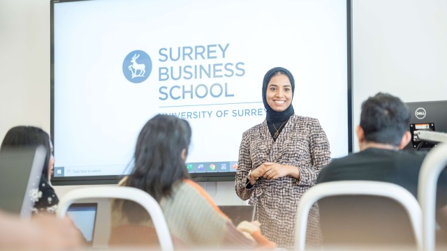 MBA lecturer standing in front of screen with Surrey Business School logo and in front of seated students