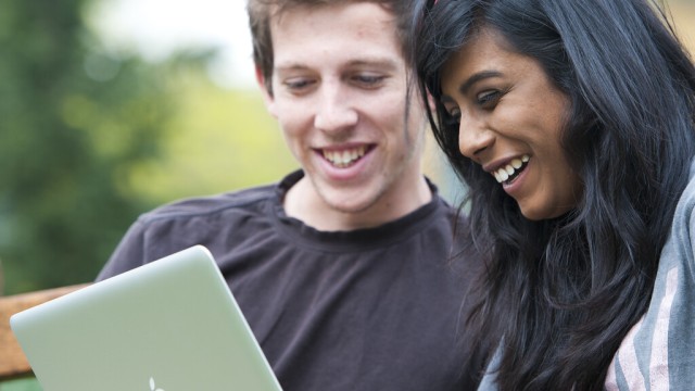 Students outside campus on bench with laptop