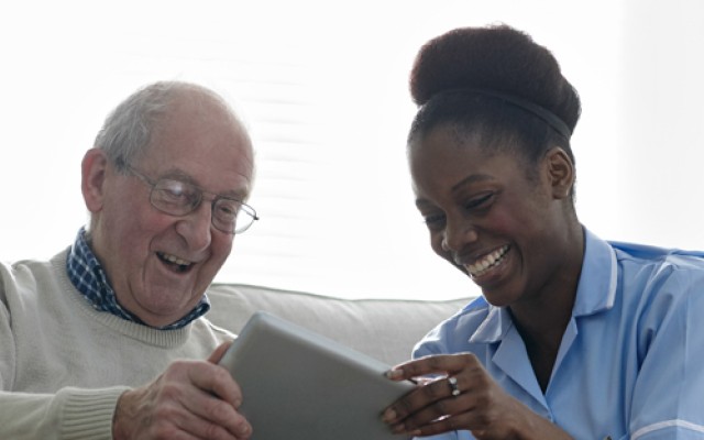 Elderly man using a tablet alongside nurse