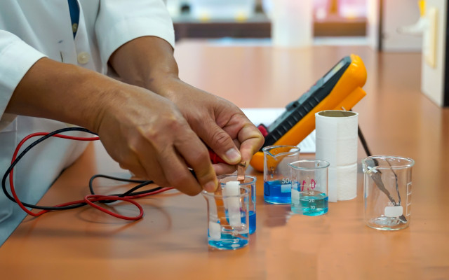 A student's hands measuring electrical currents between beakers