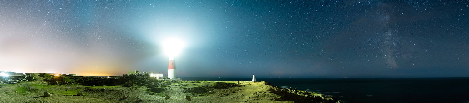 A lighthouse shining it's light into the starry night skly