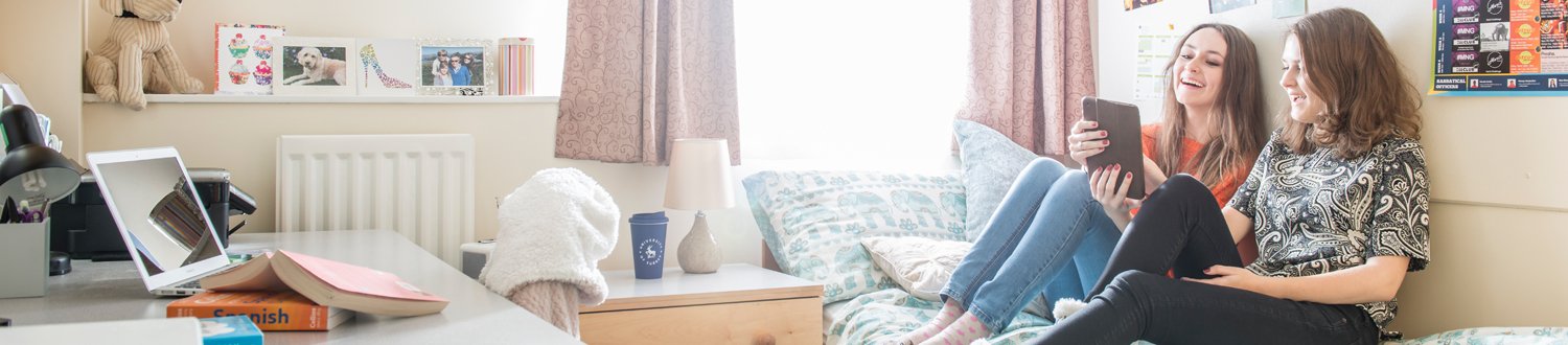 students sat on a bed looking at a tablet in Manor Park campus accommodation.