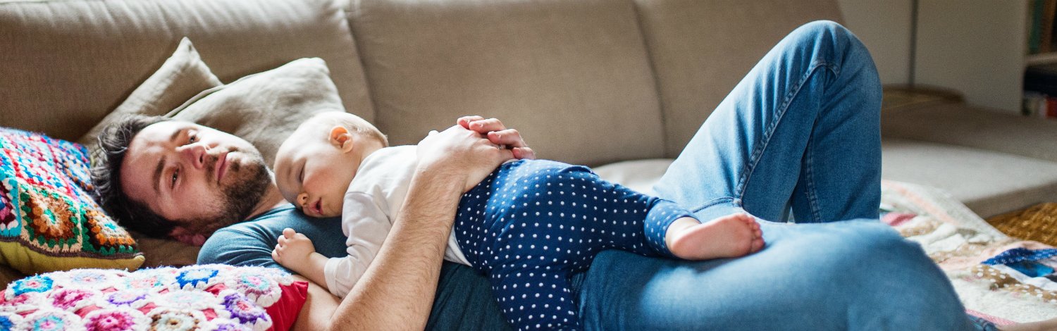 Man holding sleeping baby on sofa.