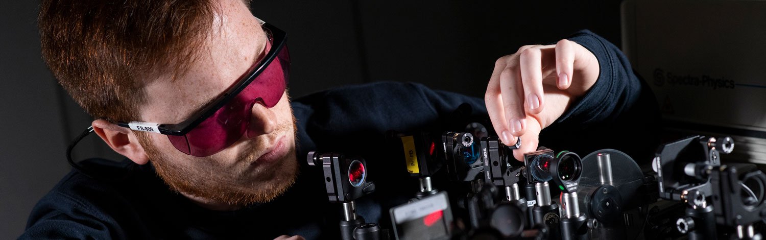 A male student wearing red glasses using equipment