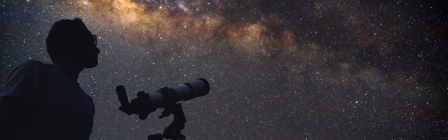 Man with telescope looking up at the starry night sky