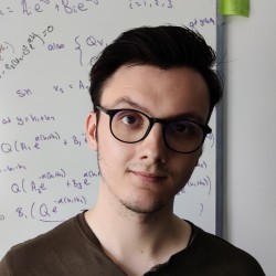 Ryan stands in front of a white board with equations, smiling at the camera.