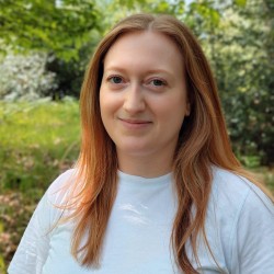 Claire, a white woman with red hair, smiles at the camera. She's wearing a white t-shirt.