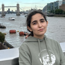 Melika, a young Iranian woman, smiles at the camera with Tower Bridge in the background.