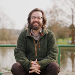 man in green jumper sat in front of lake