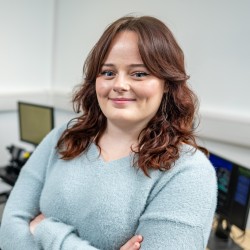 Jess smiles at the camera with her arms crossed