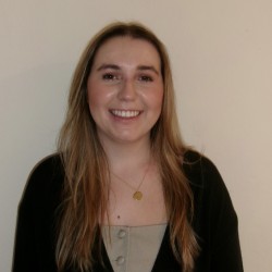 Polly stands against a light background, smiling at the camera.
