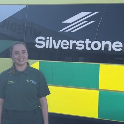 Amelie is in her paramedic uniform standing in front of an ambulance with 'Silverstone' on the side
