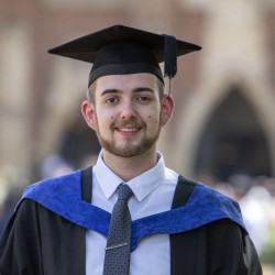 Connor is wearing his graduation gown and cap, smiling at the camera.